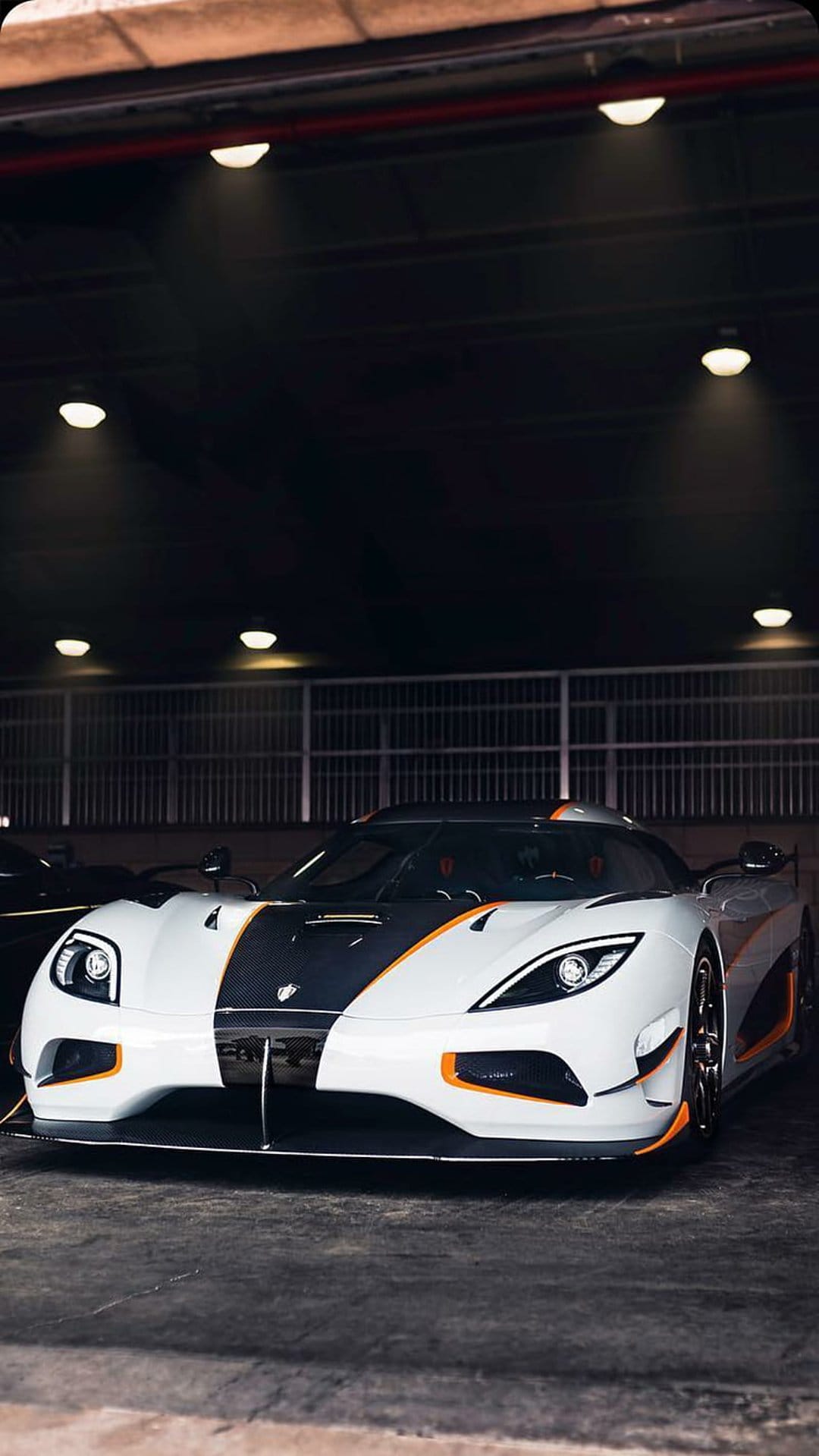 Koenigsegg Agera RS hypercar in a dark garage featuring white paint, black accents, and orange trim details.