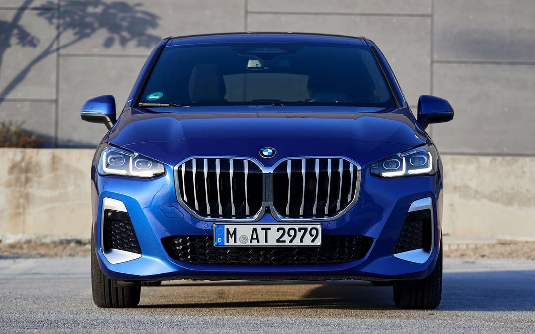 Blue BMW 2 Series Active Tourer front view with chrome grille and LED headlights against a grey wall.