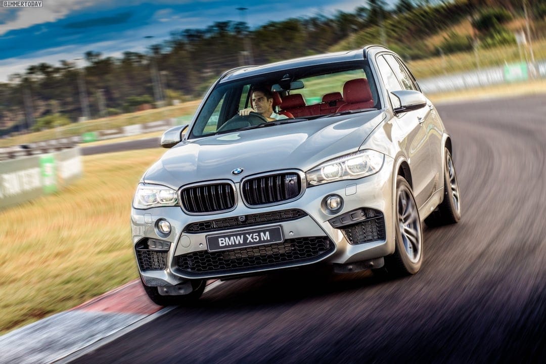 Silver BMW X5 M performance SUV speeding on a curved racetrack with motion blur background and a driver inside.