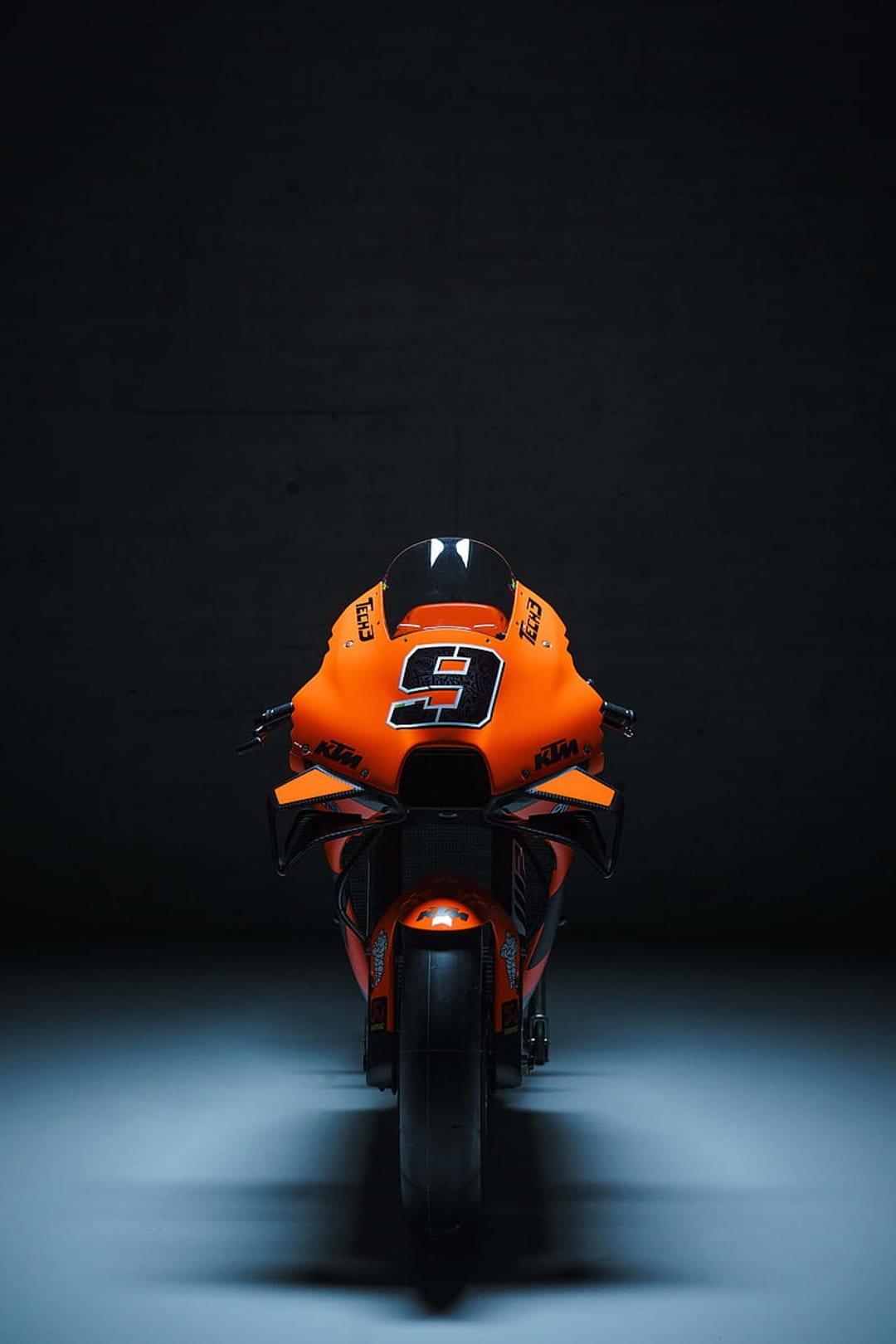 Orange KTM racing motorcycle with number 9 on the front fairing in a dark studio with dramatic lighting.