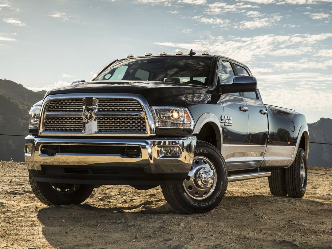 Black Ram 3500 dually pickup truck with chrome accents parked on a desert trail under a bright cloudy sky.