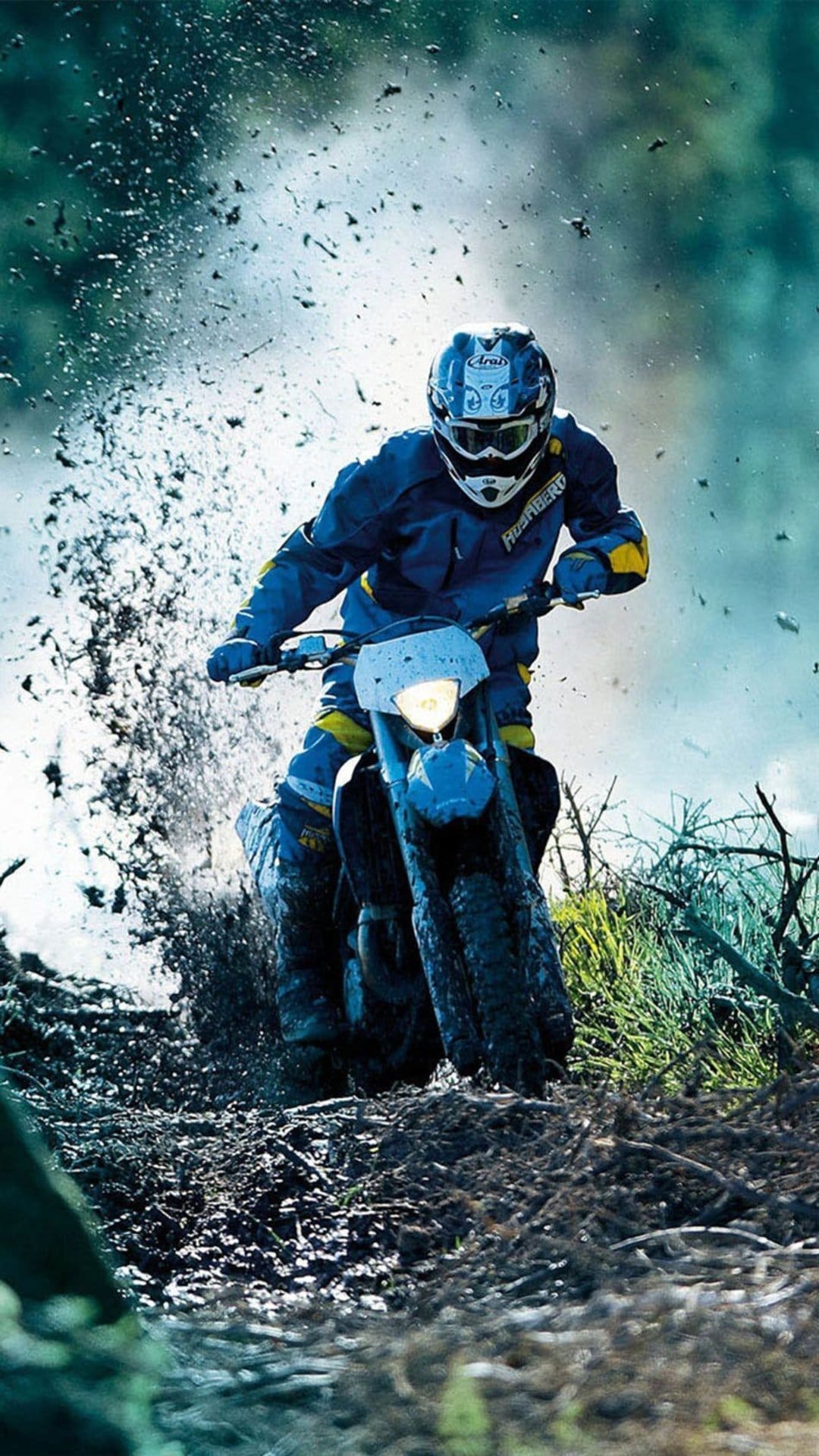 Dirt bike rider in blue gear sprays mud and water across a rugged off-road track during an intense race.