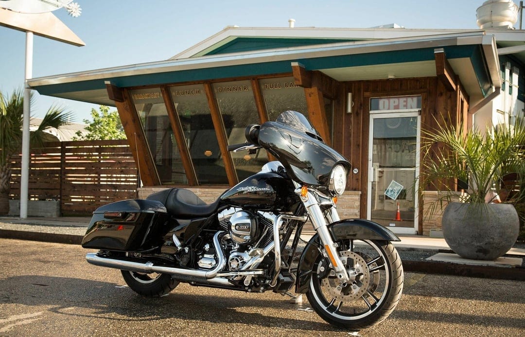 Black Harley-Davidson motorcycle parked in front of a wooden roadside diner with breakfast and lunch signs.