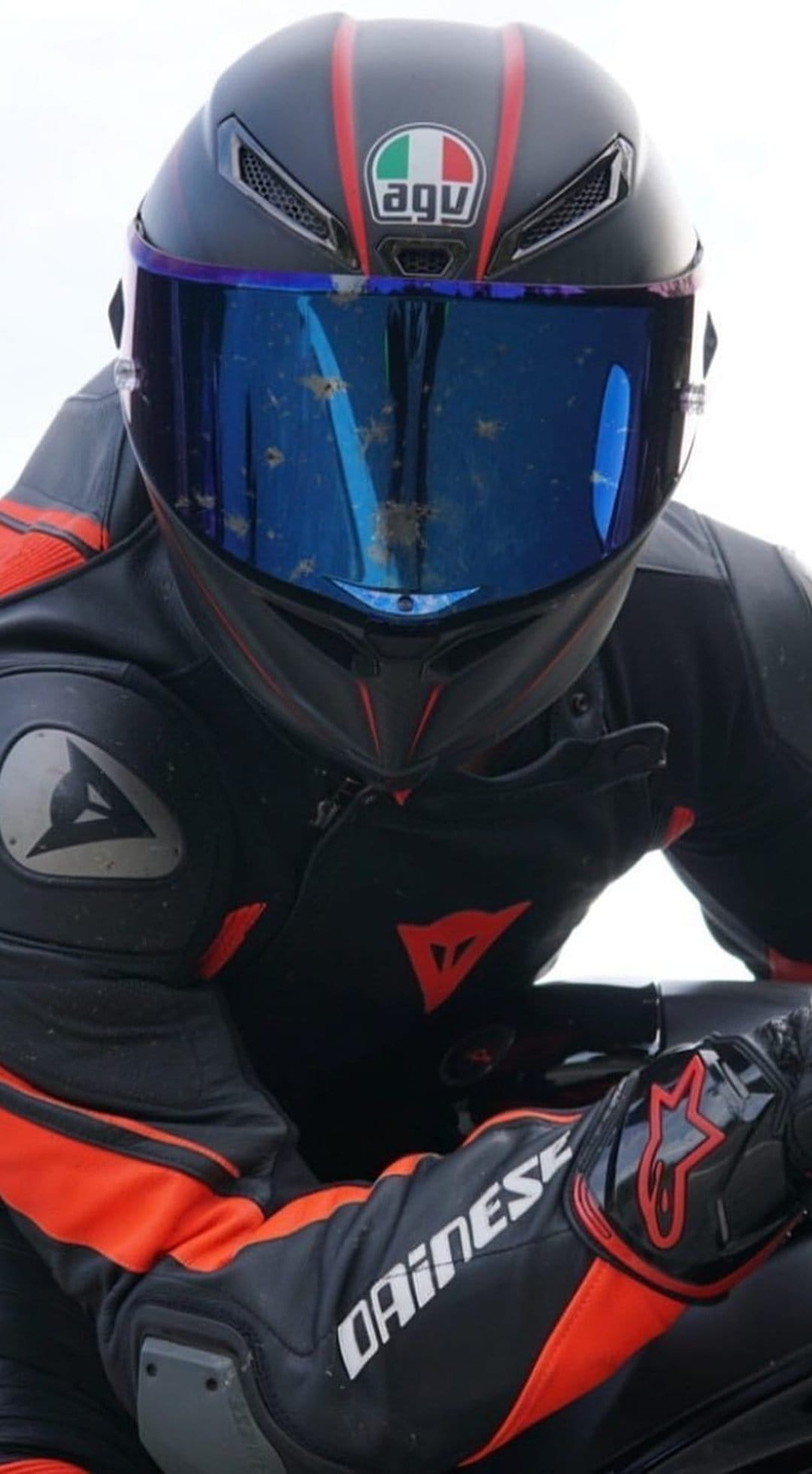 Motorcyclist in a red and black leather racing suit with a dusty blue iridescent visor on a dark helmet.