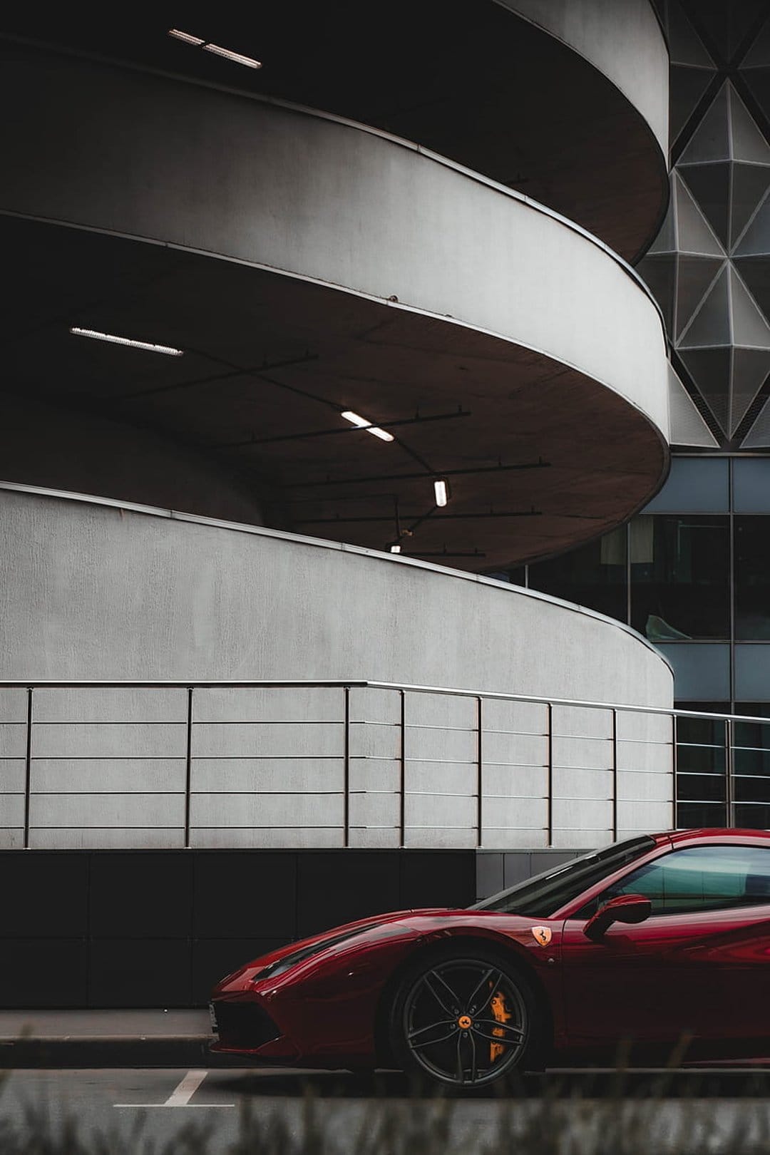 Red Ferrari sports car parked on a concrete ramp in front of a minimalist building with a geometric facade.