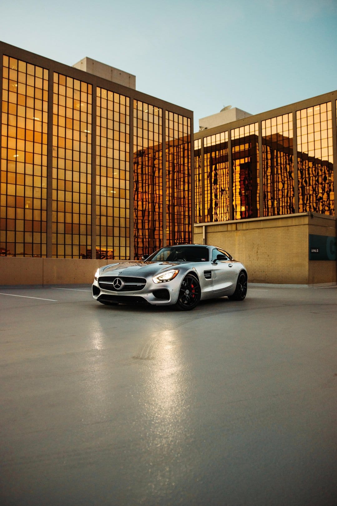 Mercedes-AMG GT sports car parked on concrete with golden glass skyscrapers reflecting warm afternoon light.
