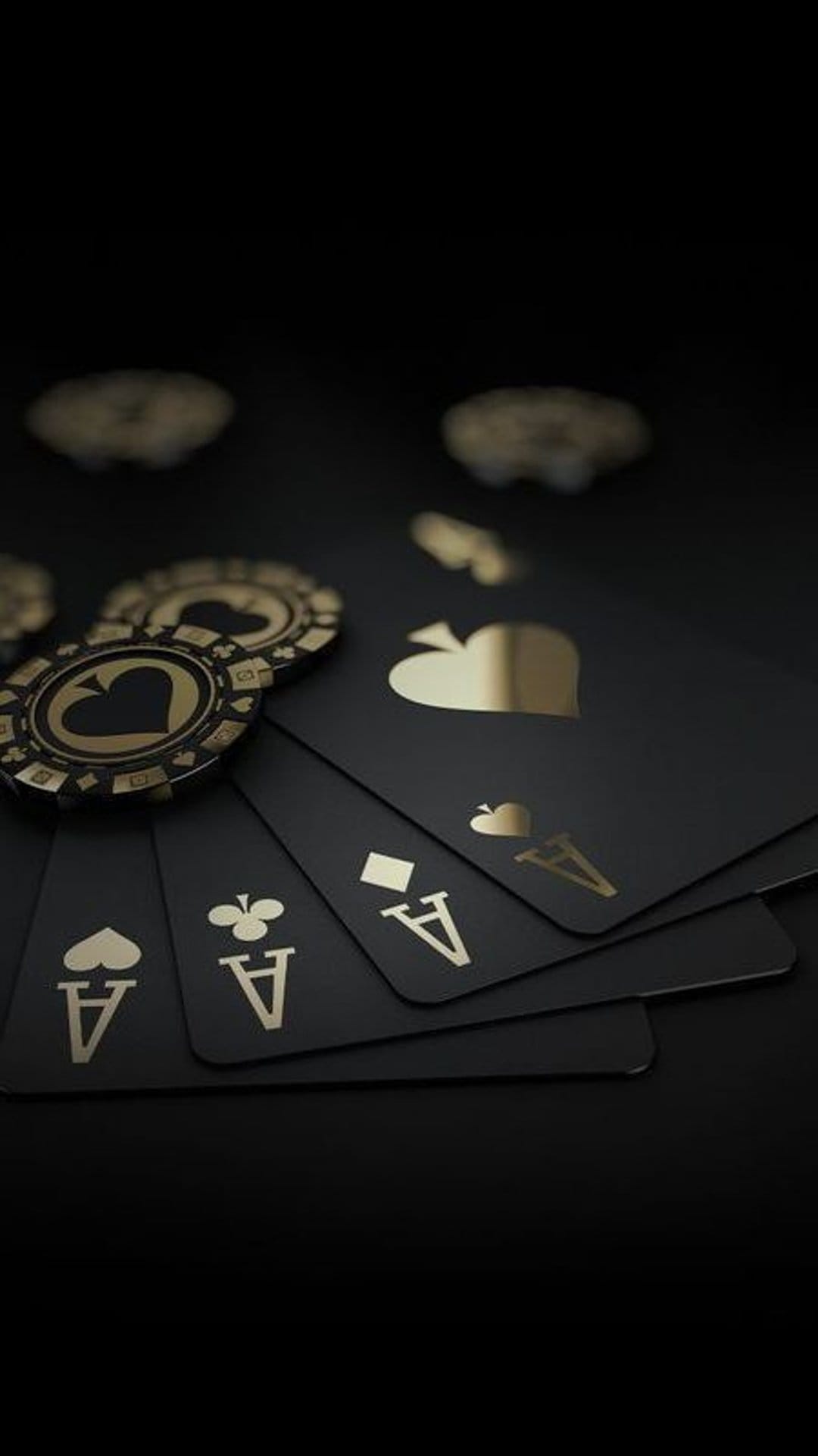 Four black ace playing cards with gold symbols underneath two metallic casino chips on a dark background.