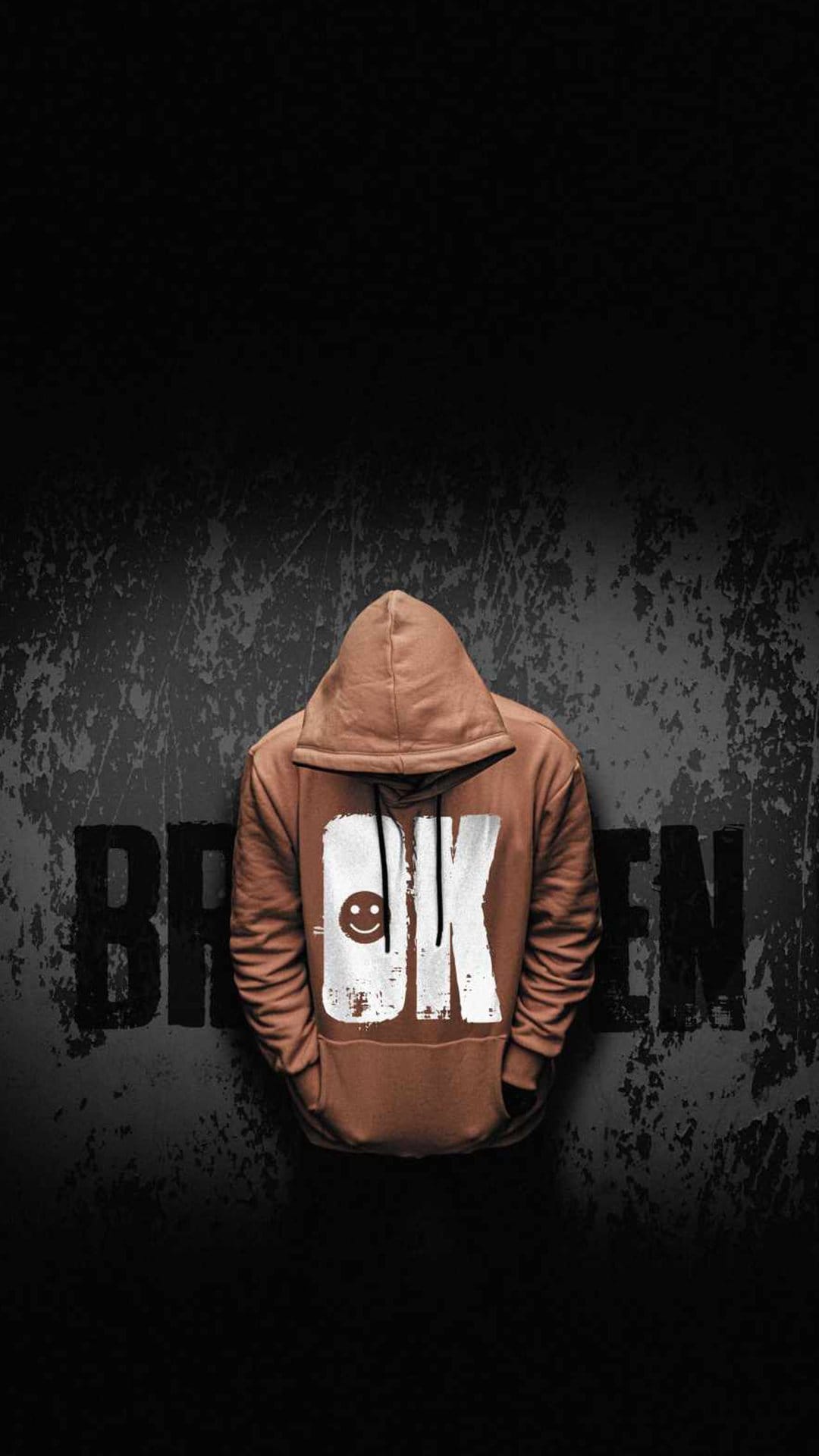 Faceless black hoodie with an OK smiley face stands against a gray concrete wall featuring broken graffiti.