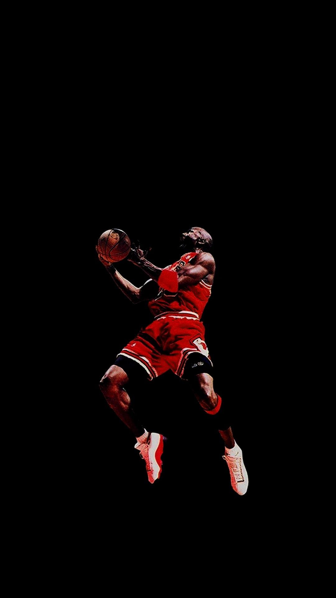 Michael Jordan in a red Bulls uniform mid-flight against a solid black background, showcasing athletic form.