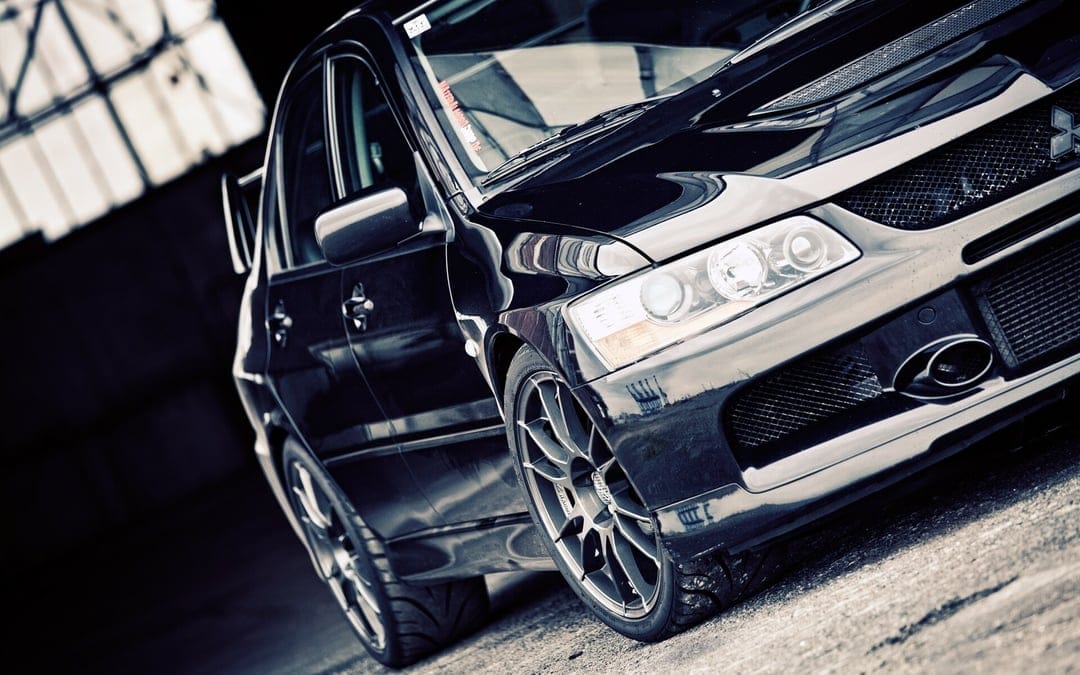 Black Mitsubishi Lancer Evolution sports car with multi-spoke rims parked in a dimly lit industrial garage.
