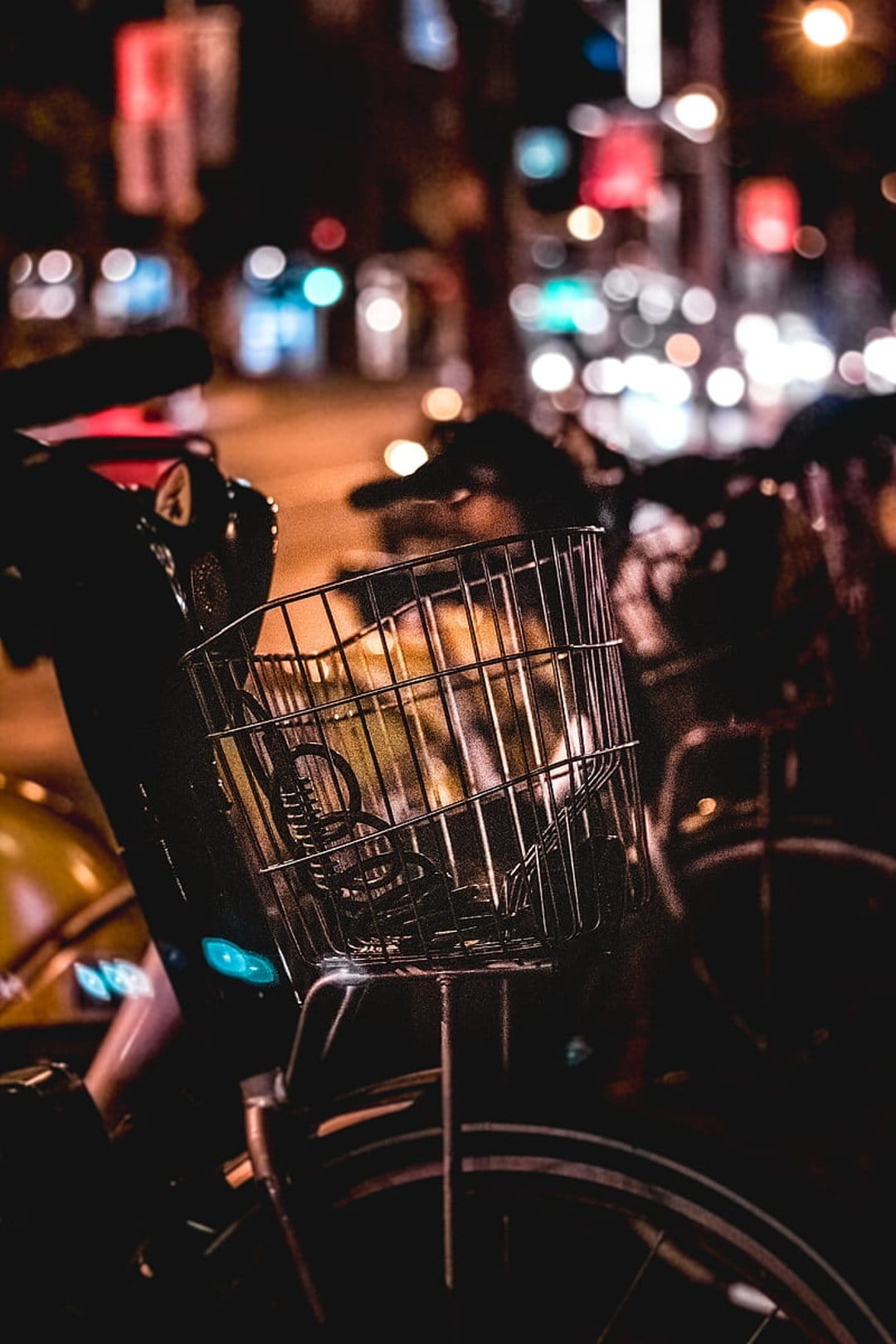 Metal bicycle basket close up against a background of glowing circular city light bokeh in the night street.