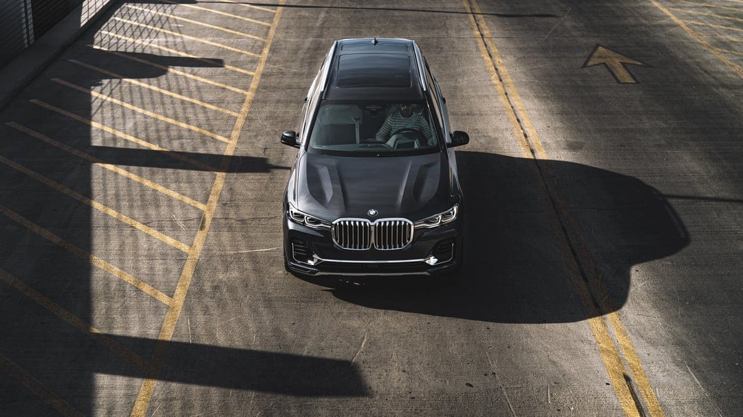 Dark grey BMW X7 SUV centered in a parking lot with yellow lines and dramatic long shadows.