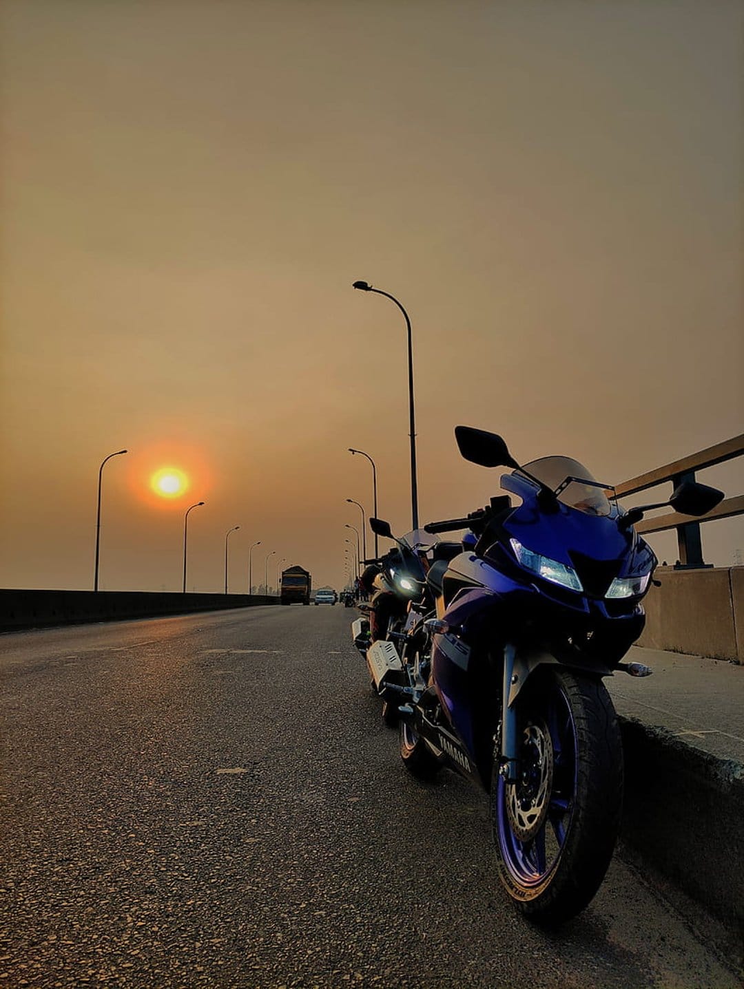 Blue and dark Yamaha sport bikes parked on a bridge against a vibrant golden hour sky and a glowing sun.