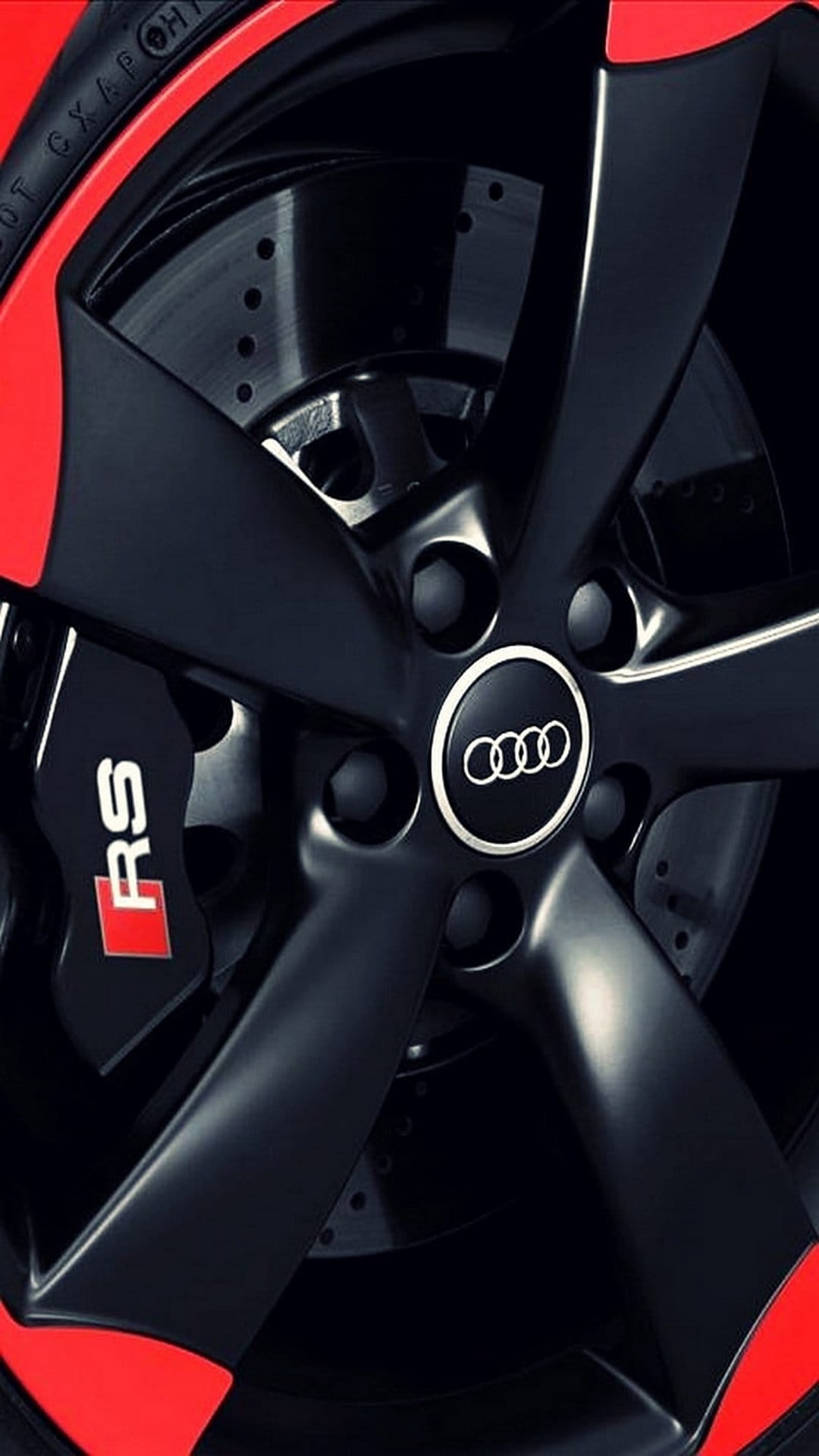 Matte black Audi RS wheel with red calipers and branding against a dark, industrial automotive background.
