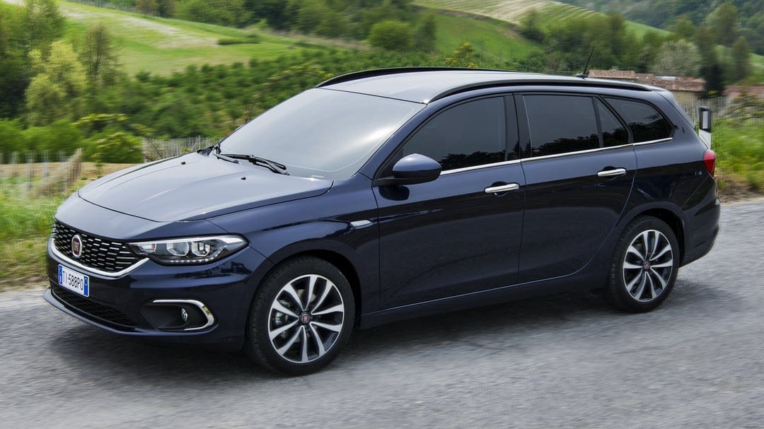 Dark blue Fiat Tipo Station Wagon driving on a gravel road with a blurred green hillside background.