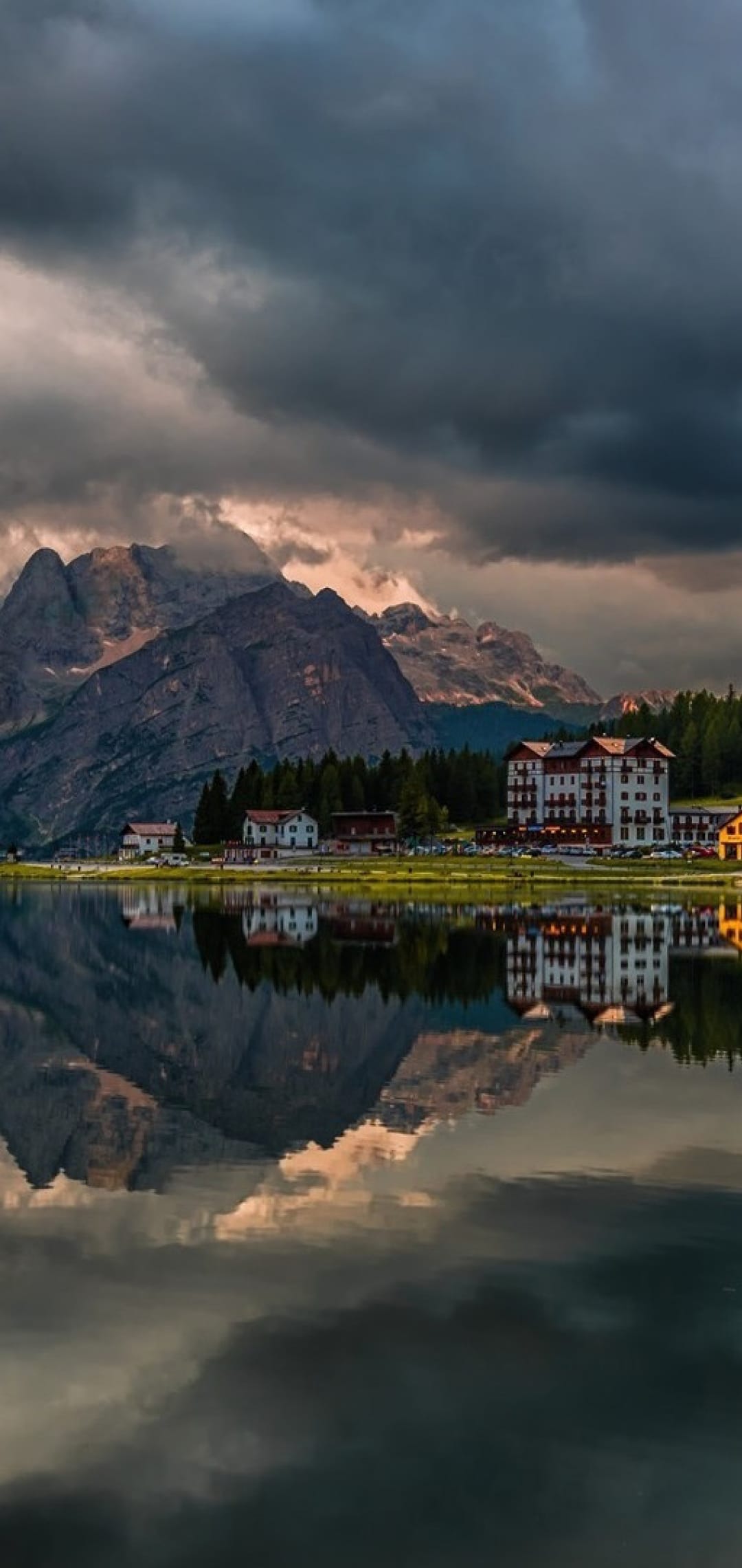 Grand Hotel Misurina and jagged Dolomite mountain peaks reflected in the still surface of a clear alpine lake.
