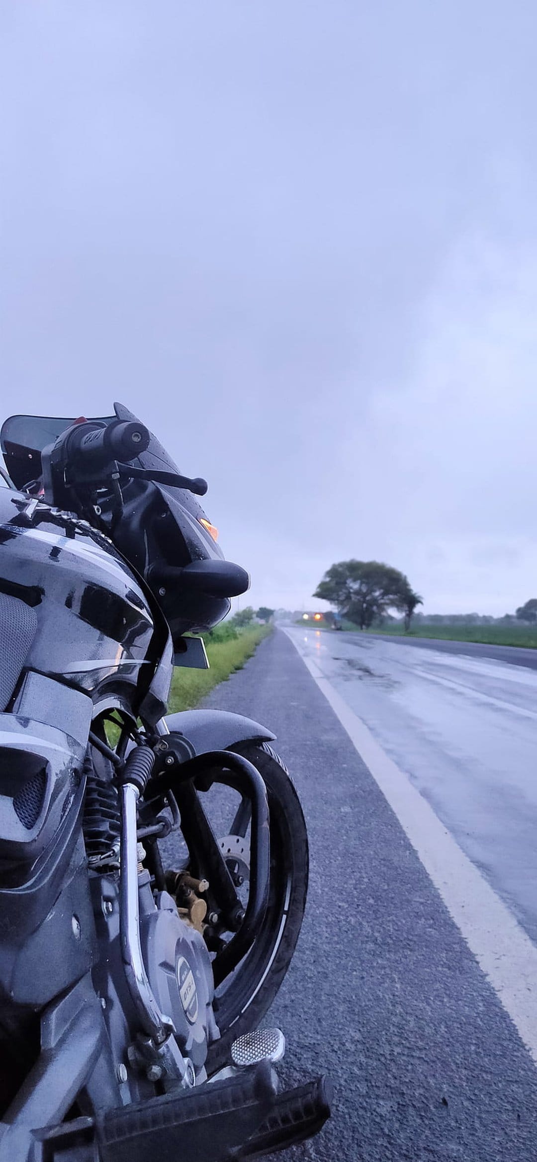 Black motorcycle parked on wet asphalt during an overcast day with reflections of light on the road surface.