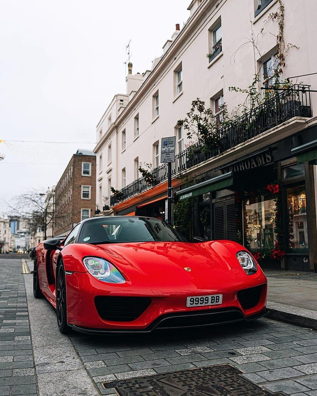 Red Porsche 918 Spyder supercar parked on a cobblestone London street with white stucco buildings in background.