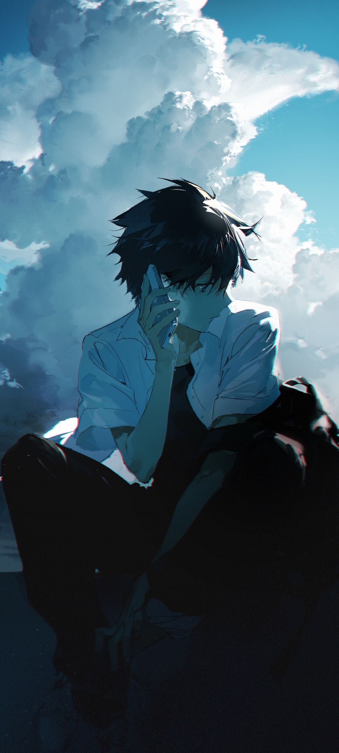 Young man with dark hair talks on a phone beneath massive white clouds and a vibrant blue sky in the background.