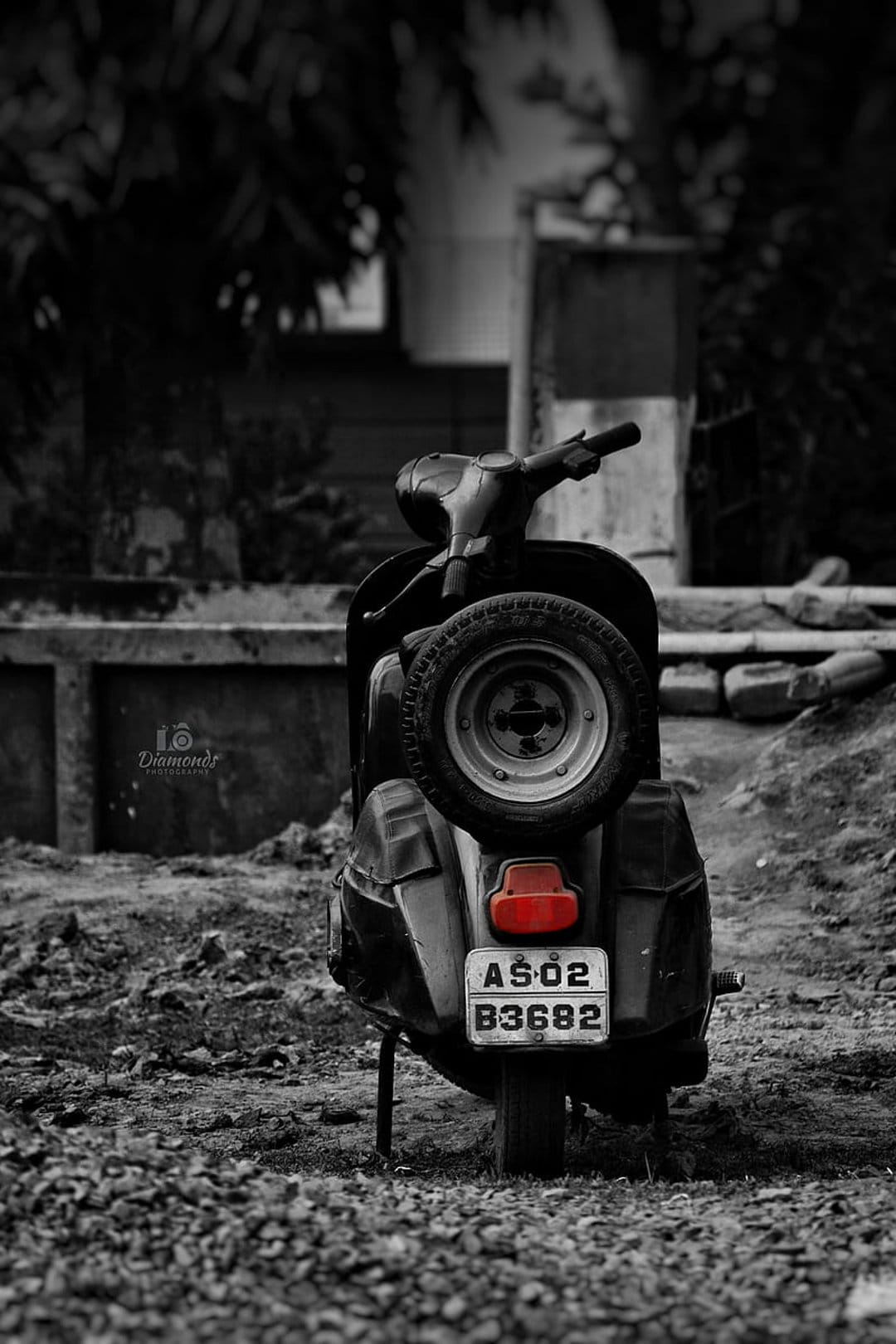 Vintage scooter with a glowing red taillight and rear spare tire parked on a grey gravel surface outdoors.