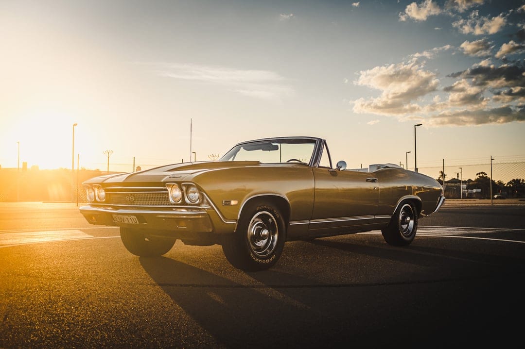 Gold 1968 Chevelle SS convertible parked on asphalt at sunset with warm lens flare and long shadows.