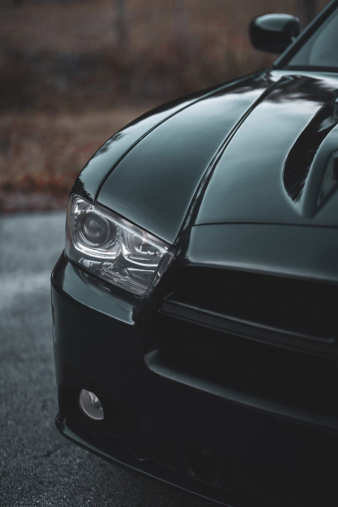 Black Dodge Charger headlight and sculpted hood with vents shown in a detailed close-up automotive shot.