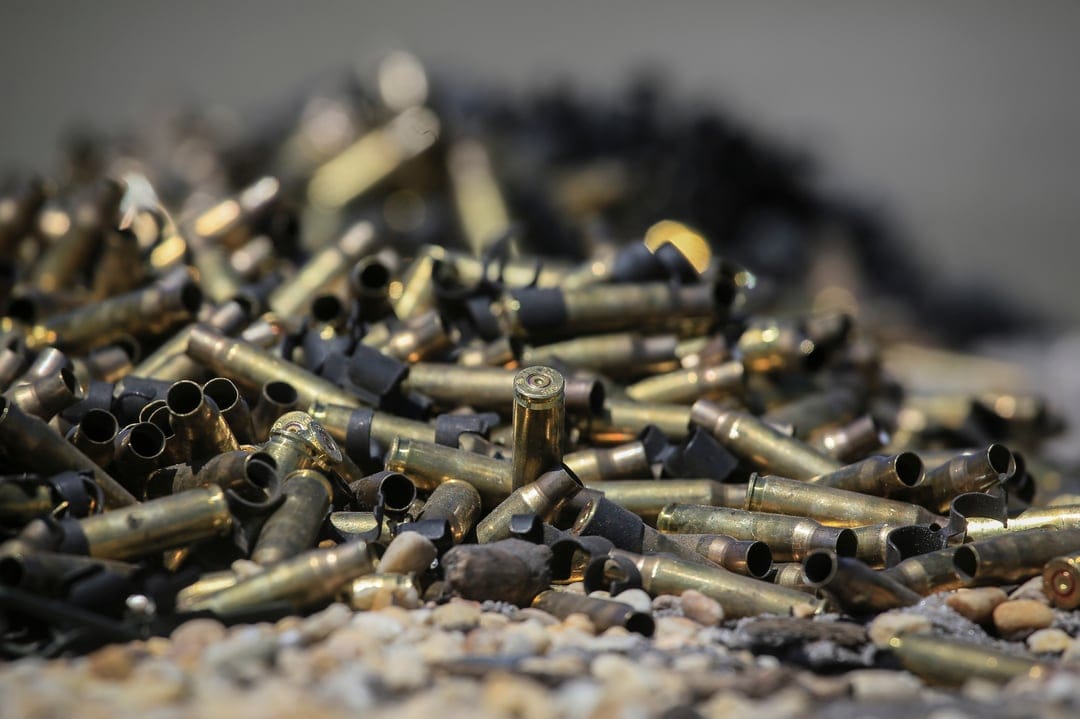 Brass ammunition shells lie on small grey stones with a focused foreground and blurred outdoor background.