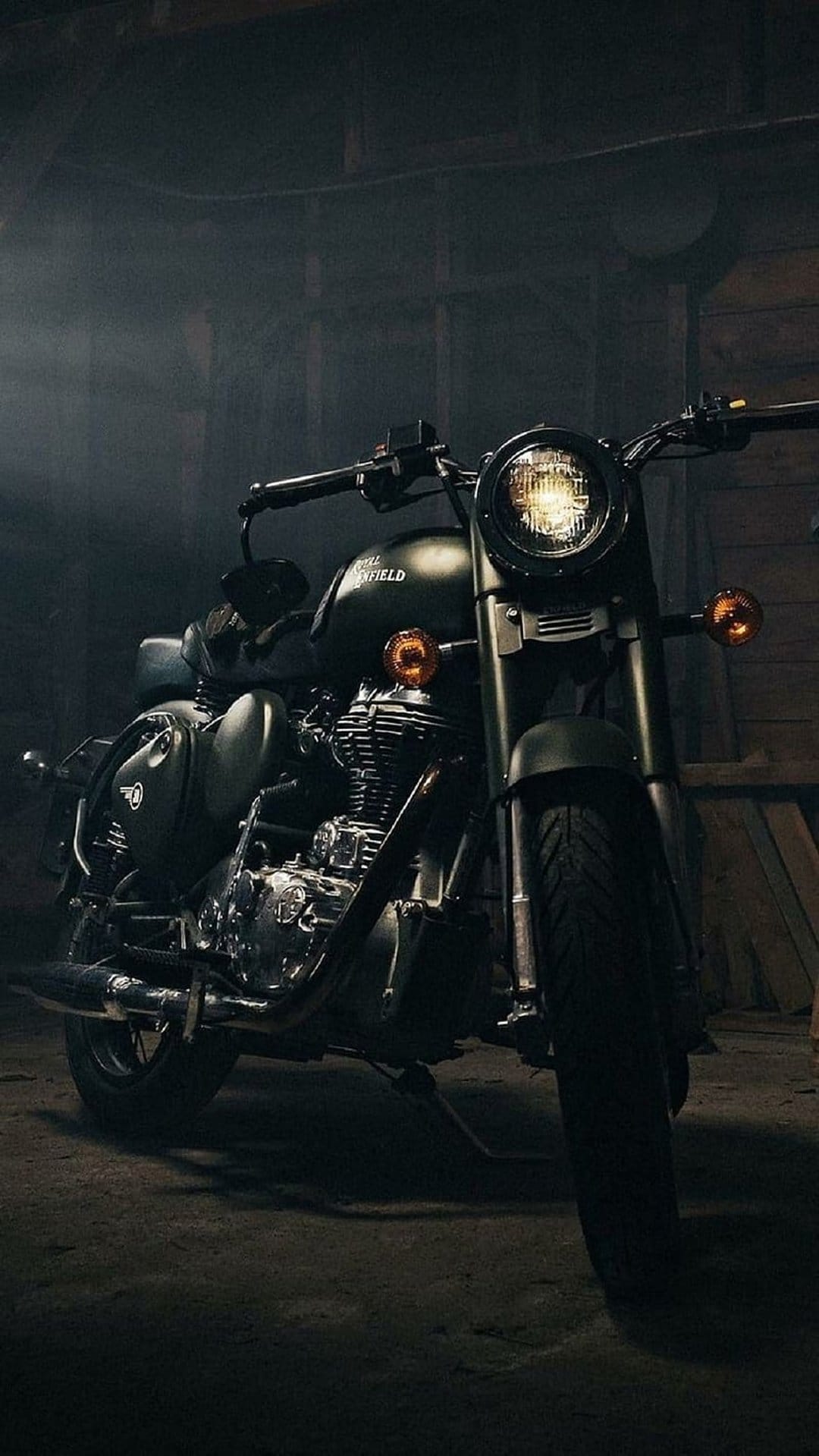 Matte green Royal Enfield motorcycle with chrome engine parts parked inside a dark wooden barn at night.