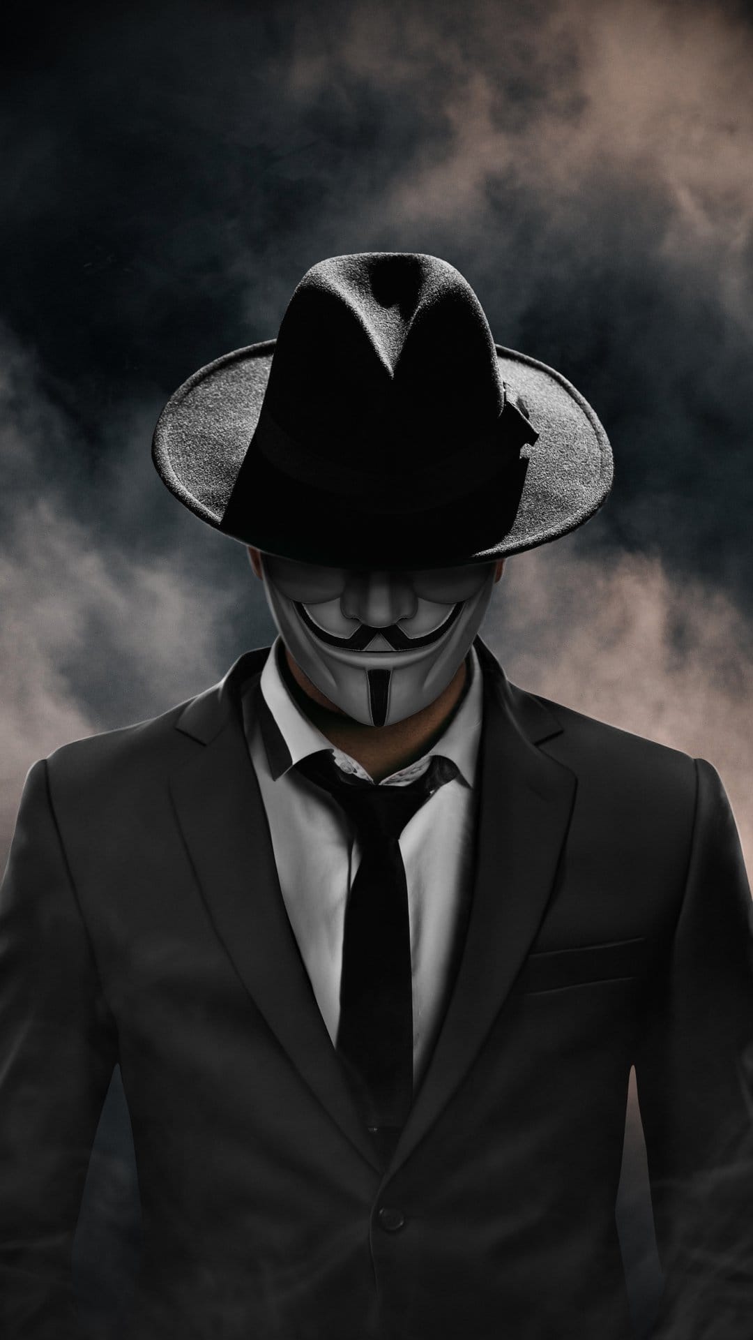 Masked figure wearing a white Guy Fawkes mask, black fedora, and suit jacket against a dark smoky background.