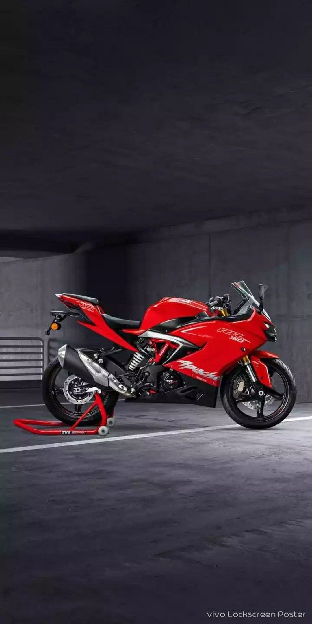 Red TVS Apache RR 310 sportbike on a matching red stand inside a dark, textured concrete garage setting.