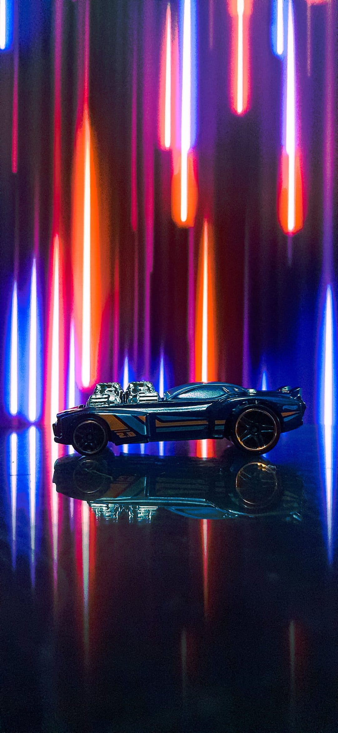 Blue Hot Wheels car with dual engines on a reflective floor against red and orange blurred neon light streaks.