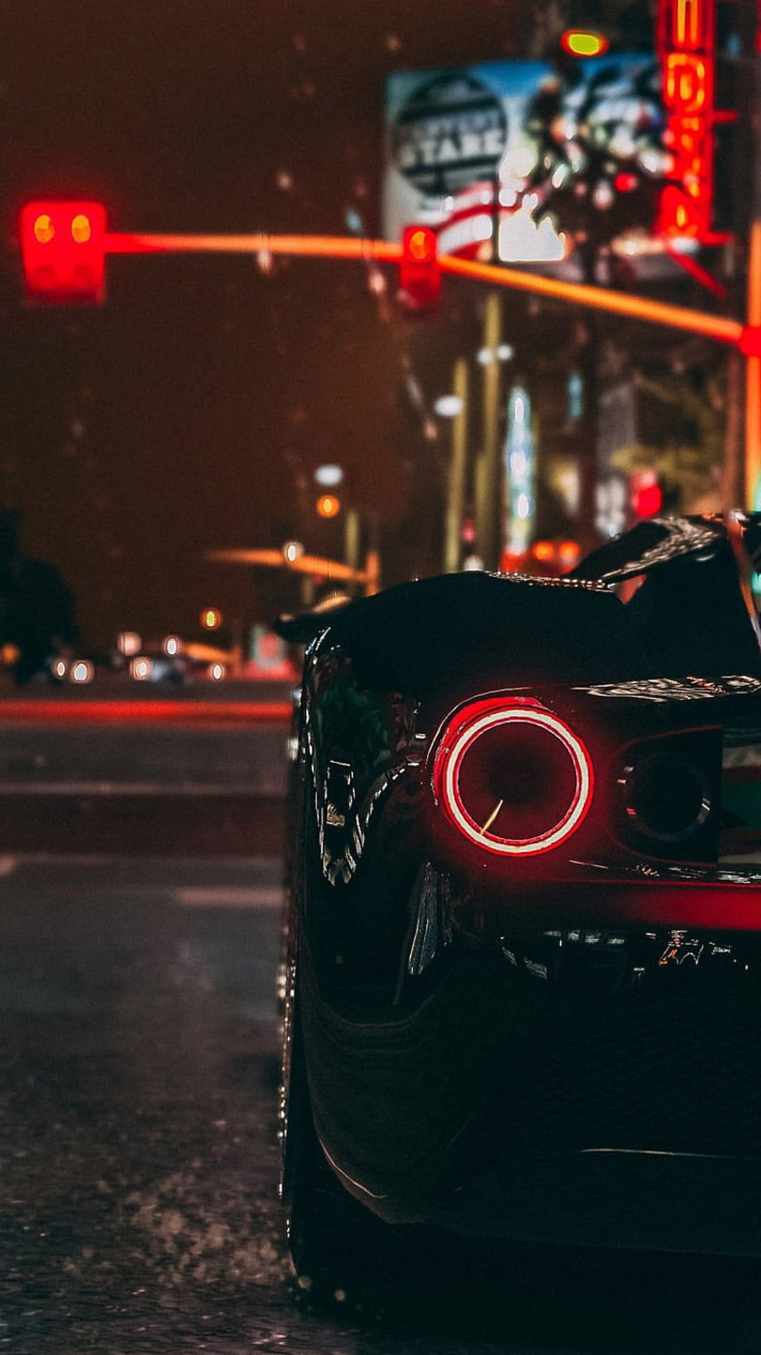 Red car taillights illuminate a wet asphalt road at night with colorful neon reflections and city lights.