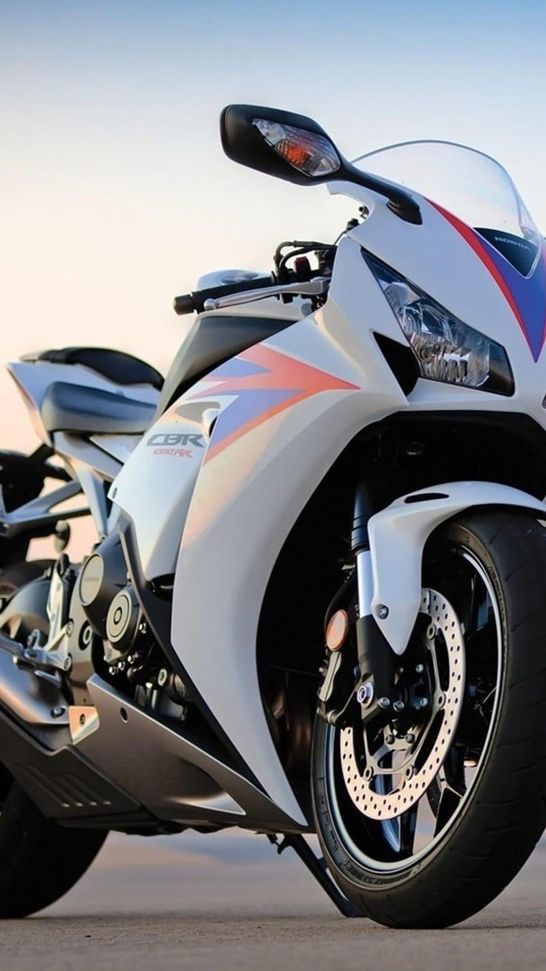 Honda CBR motorcycle with white fairings and red and blue racing stripes, showing the front wheel and engine.