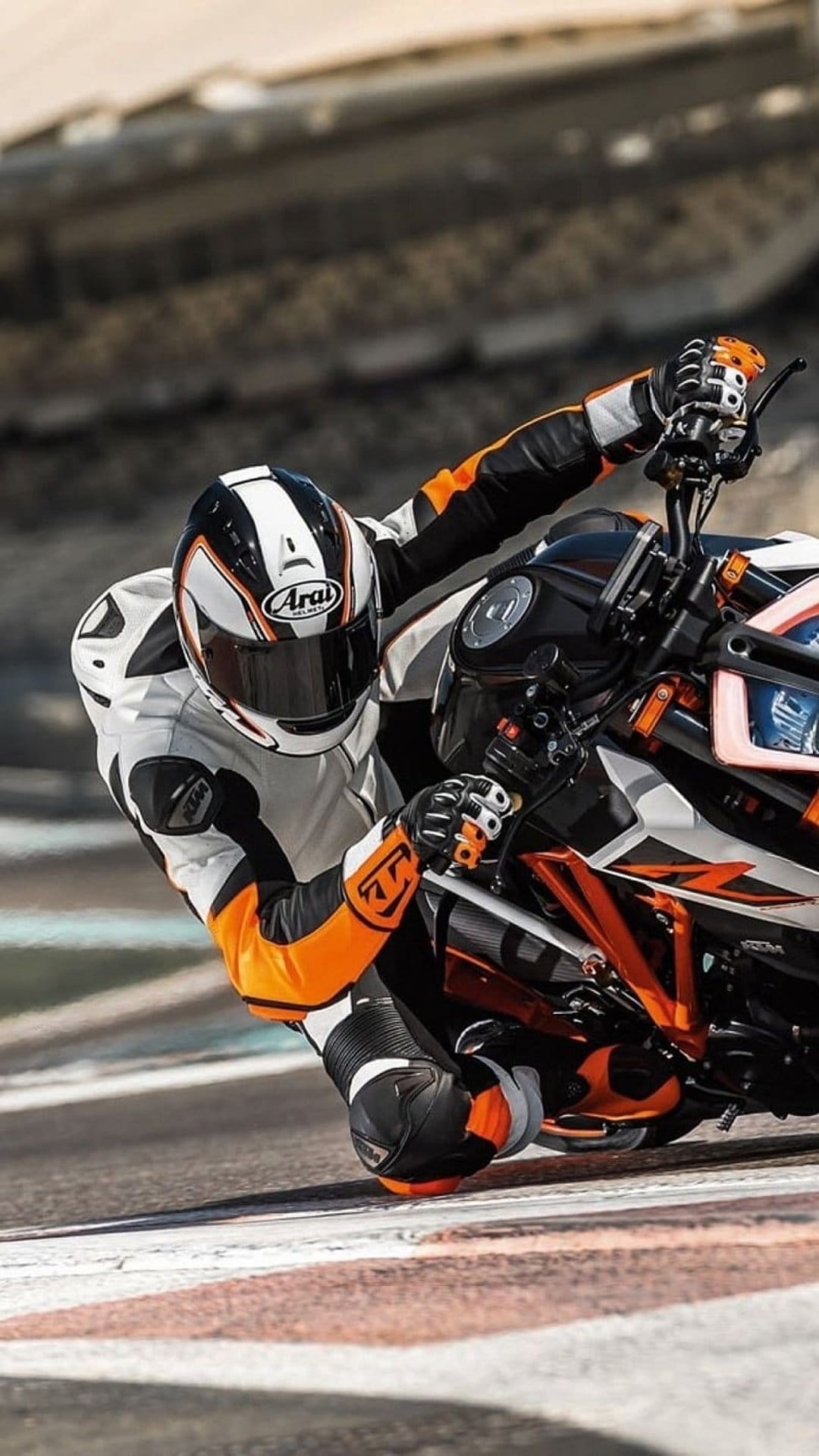Professional rider in orange leathers leans low into a turn on a paved circuit with an Arai helmet visible.