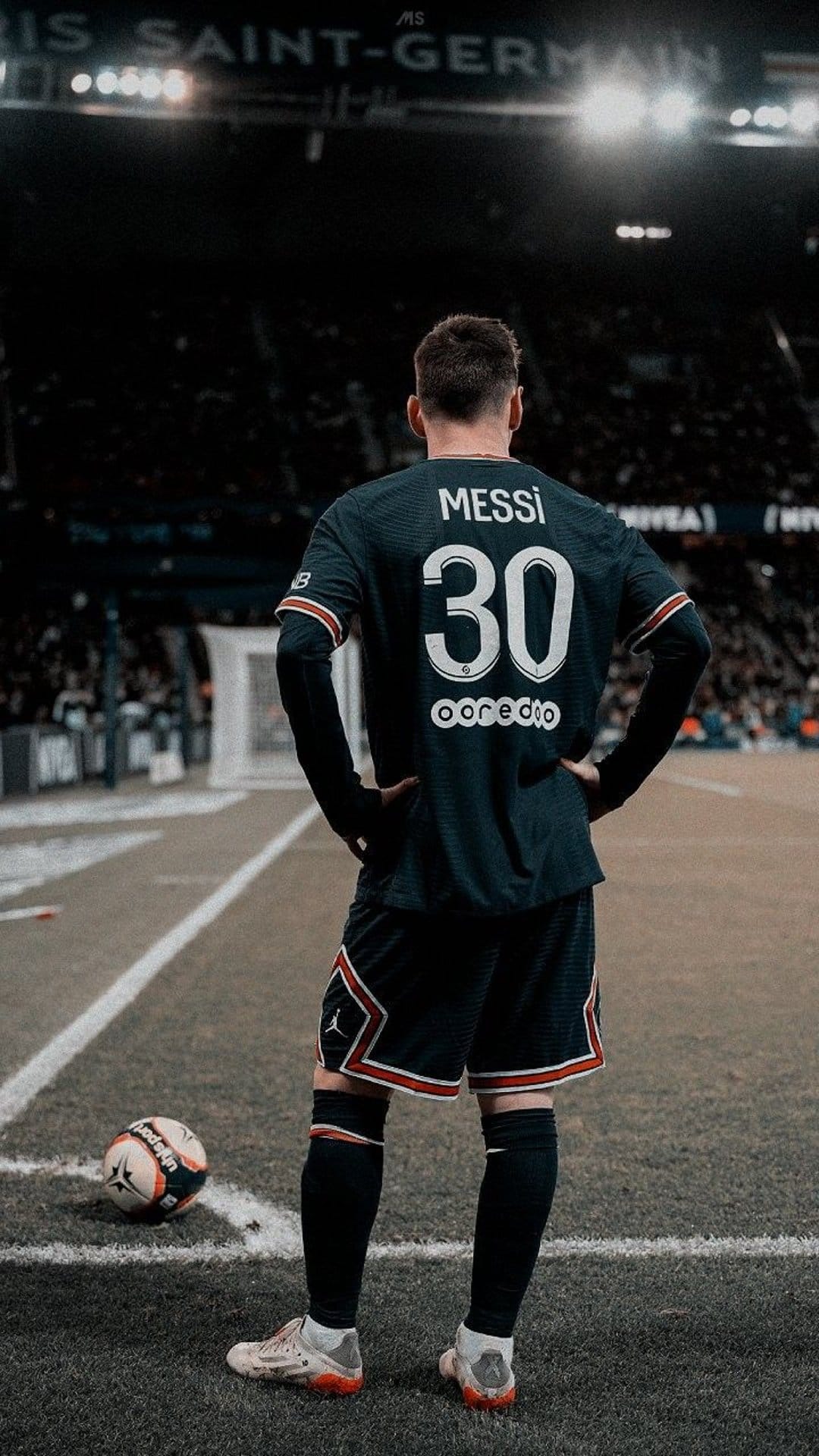Lionel Messi viewed from behind in a navy PSG kit with number 30 standing on a pitch under stadium lights.