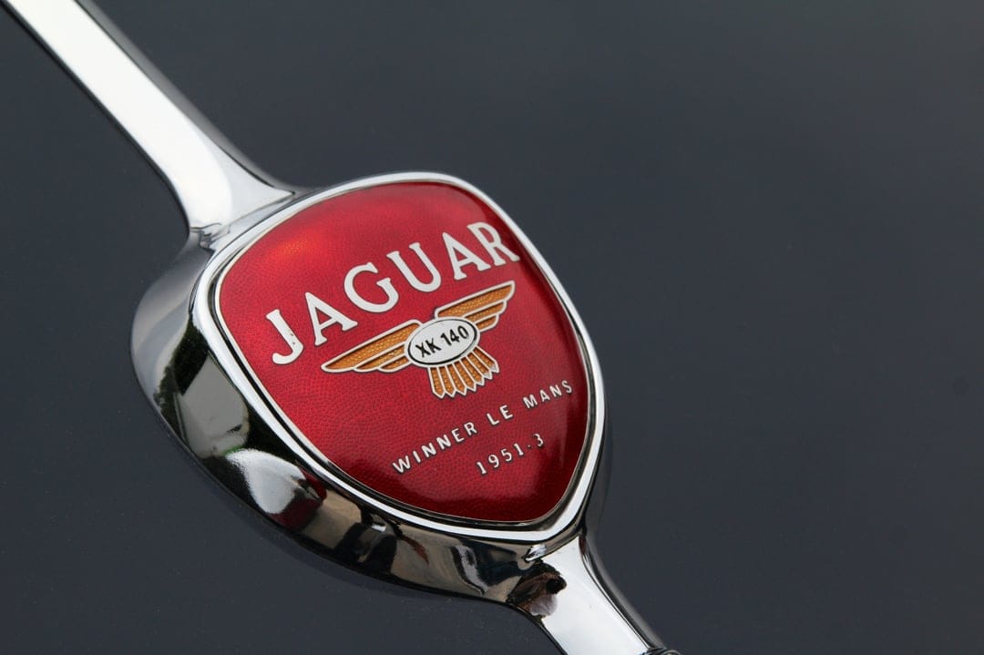 Jaguar XK 140 red emblem with chrome wings and 1951 Le Mans victory text captured in a detailed macro shot.