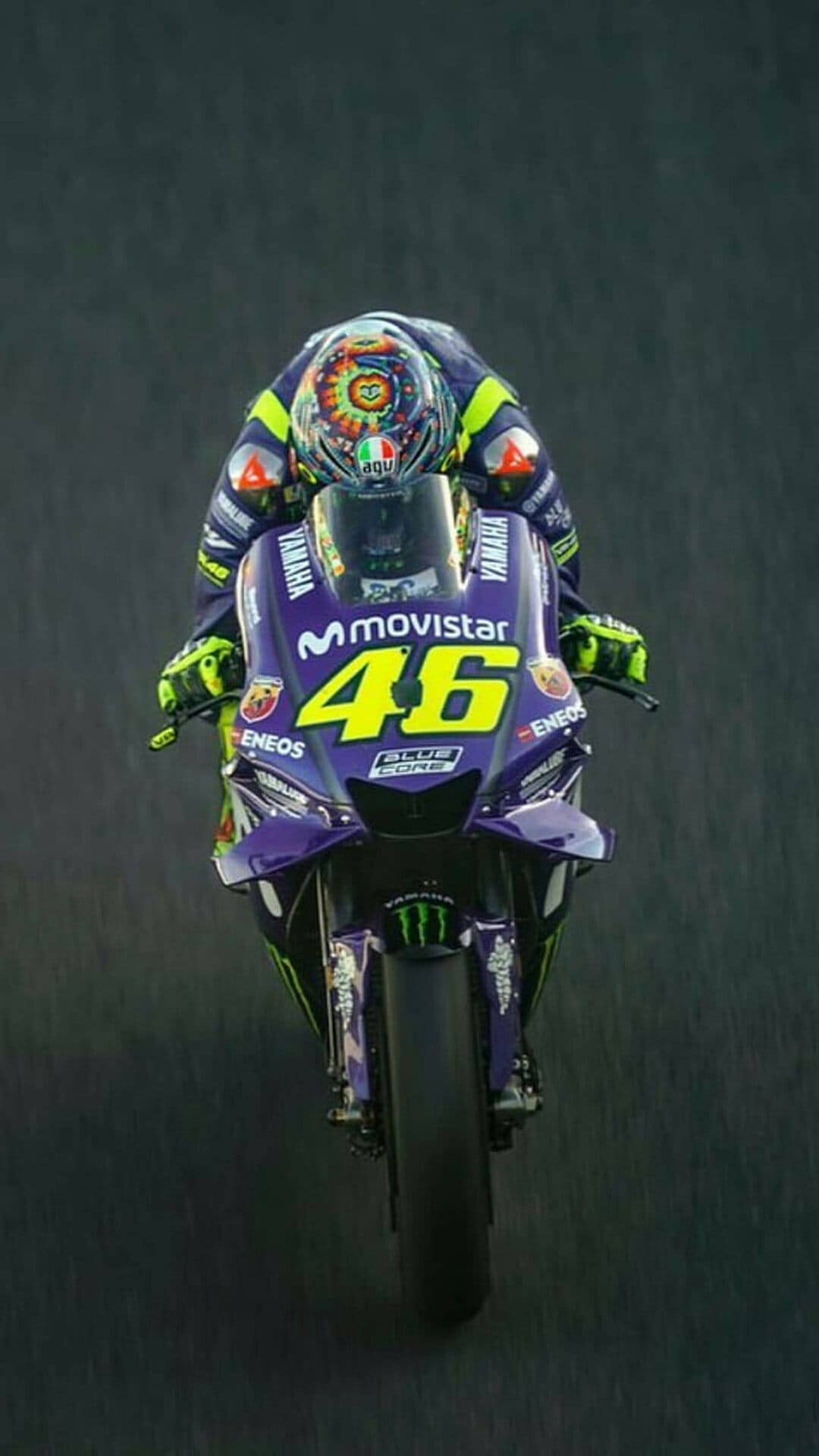 Valentino Rossi leans a blue Yamaha motorcycle on a race track wearing a yellow and blue suit with number 46.