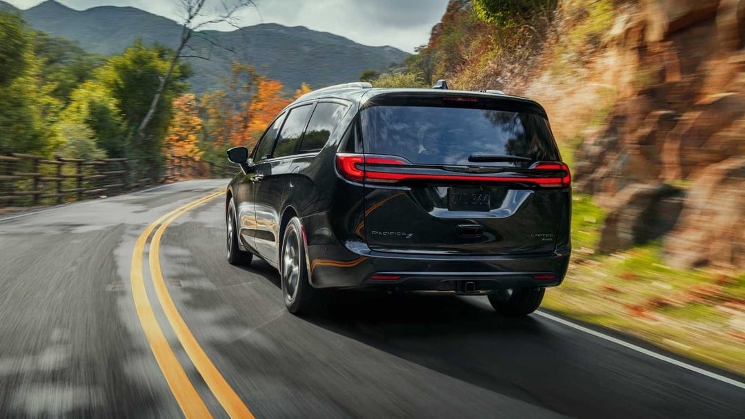 Black Chrysler Pacifica driving on a winding mountain road with autumn trees and rocky cliffside backgrounds.
