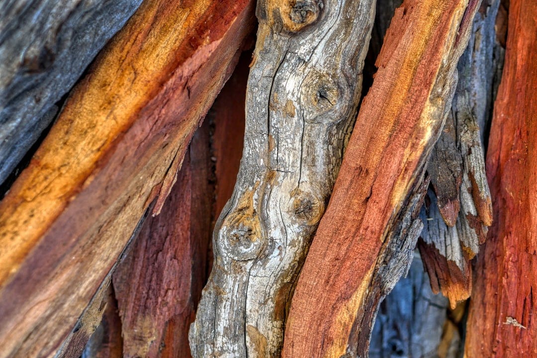 Stacked firewood pieces with visible grain, knots, and textures in shades of red, orange, and weathered gray.