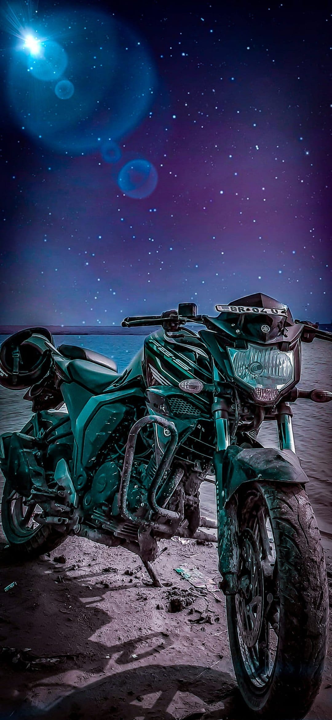 Dark green sportbike with a helmet on its seat parked on a sandy shore beneath a purple starry nebula sky.