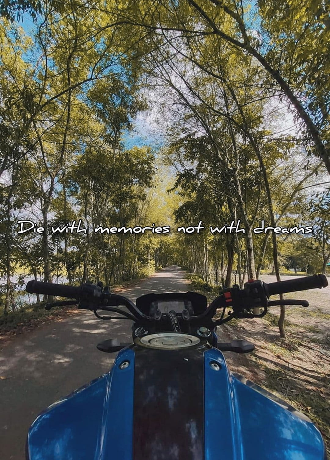 Blue motorcycle handlebars frame a tree-lined road with the text Die with memories not with dreams overlaid.