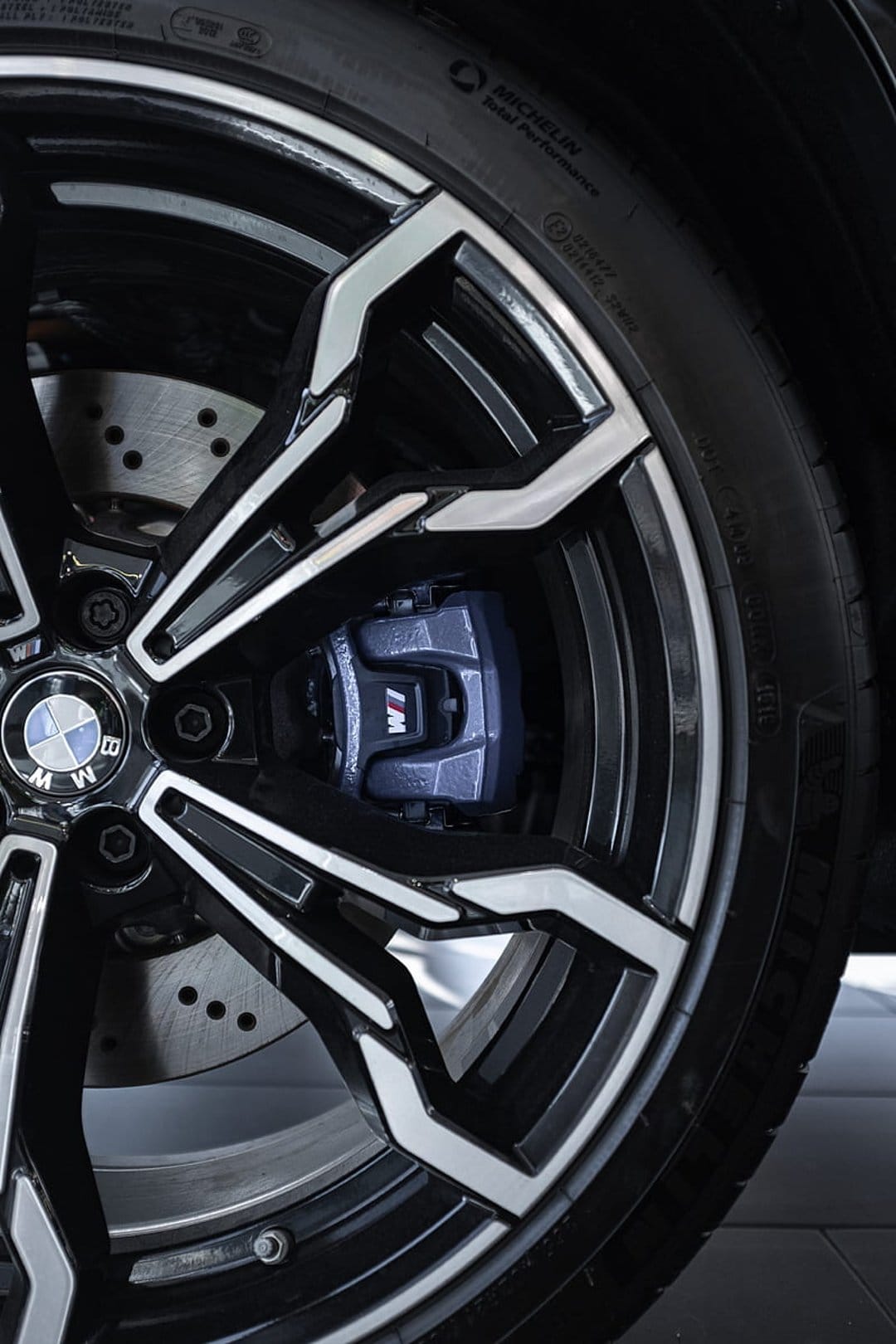 BMW M Sport alloy wheel rim featuring a bright blue brake caliper and textured Michelin performance tire tread.