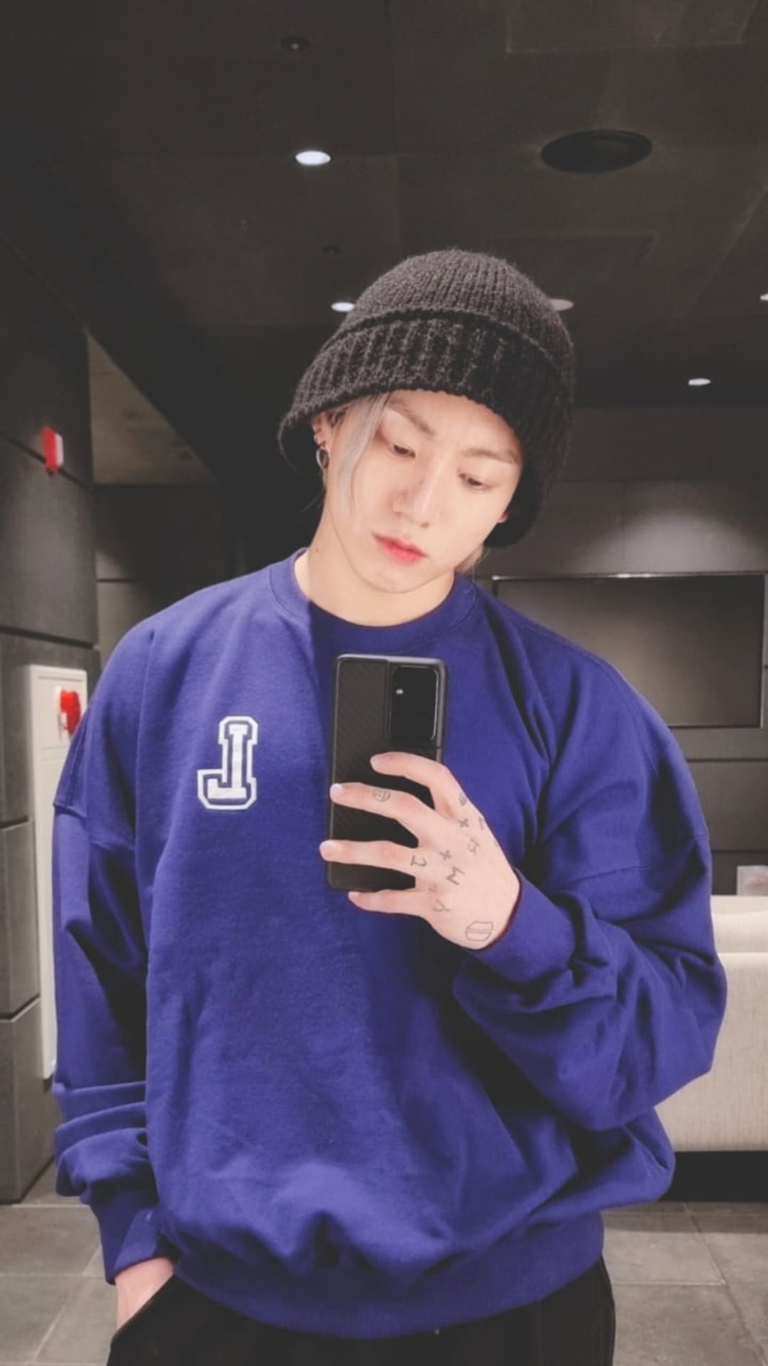 Jungkook of BTS in a purple sweatshirt and black beanie holding a phone for a mirror selfie vertical portrait.