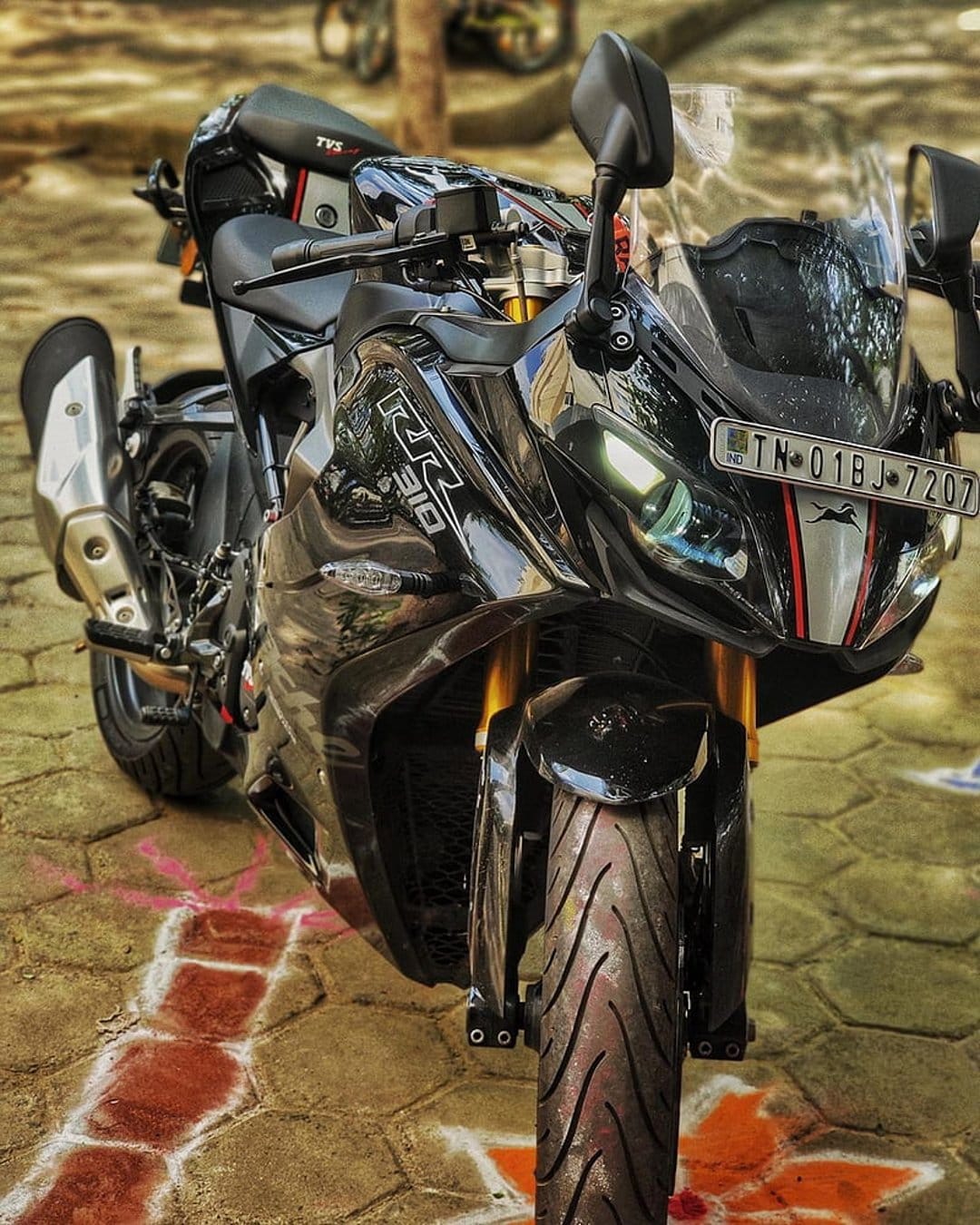 TVS Apache RR 310 motorcycle with gold forks and LED headlights parked on pavement with colorful chalk art.