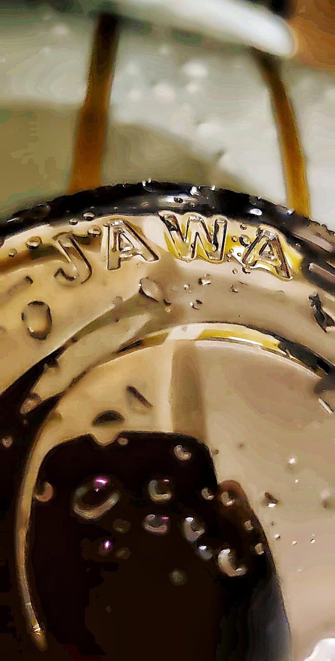 JAWA logo embossed on a curved metallic surface covered in clear water droplets with sharp light reflections.