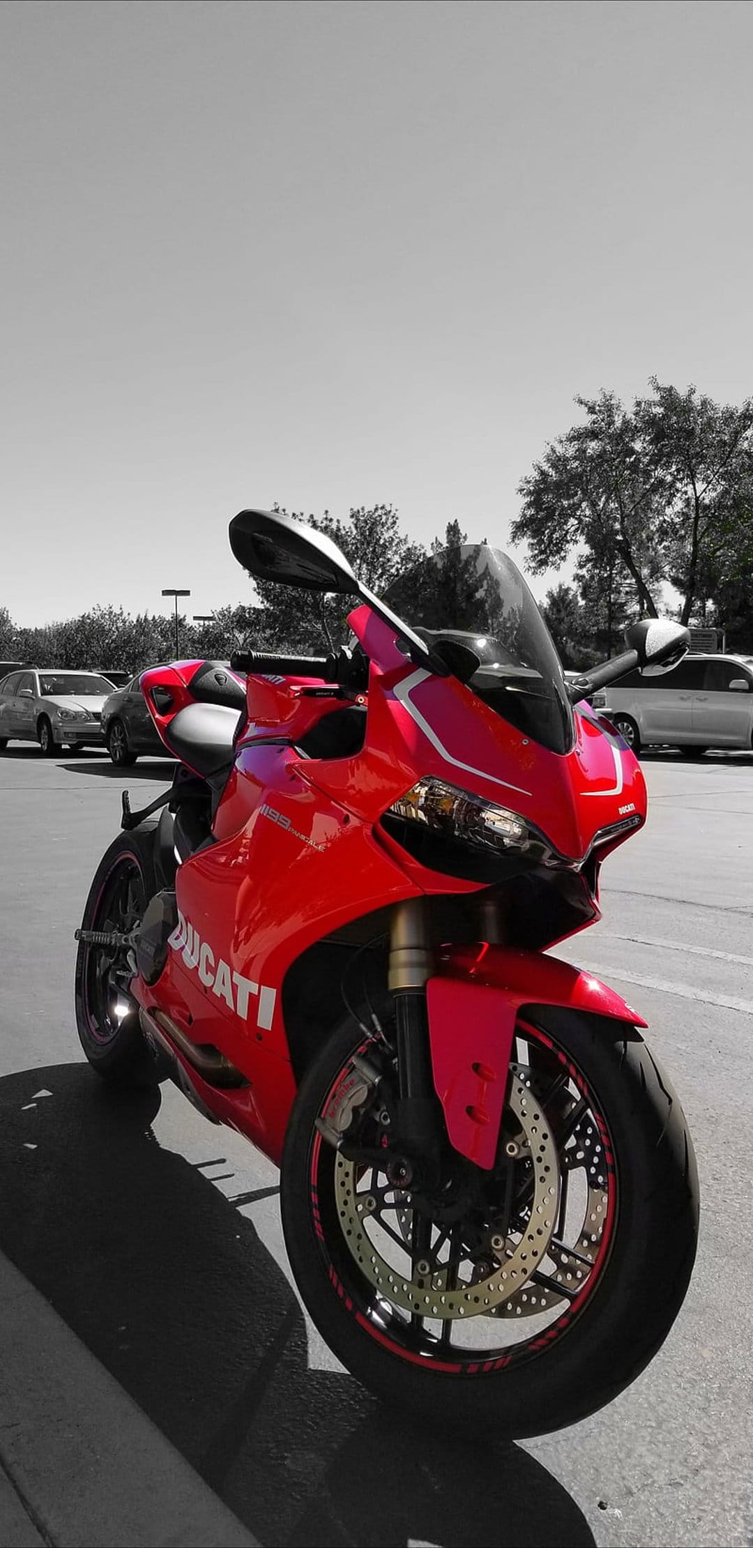Red Ducati motorcycle with aerodynamic fairings parked outdoors against a blurred grayscale city background.