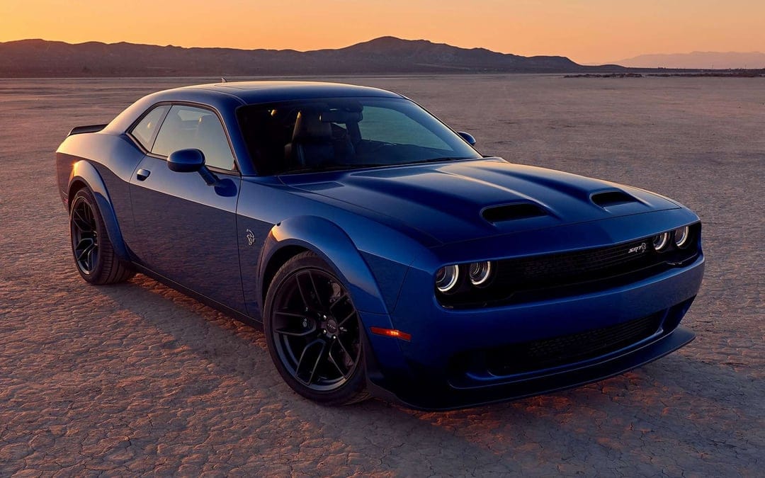 Blue Dodge Challenger SRT Hellcat on a cracked desert floor with mountains and a sunset sky background.