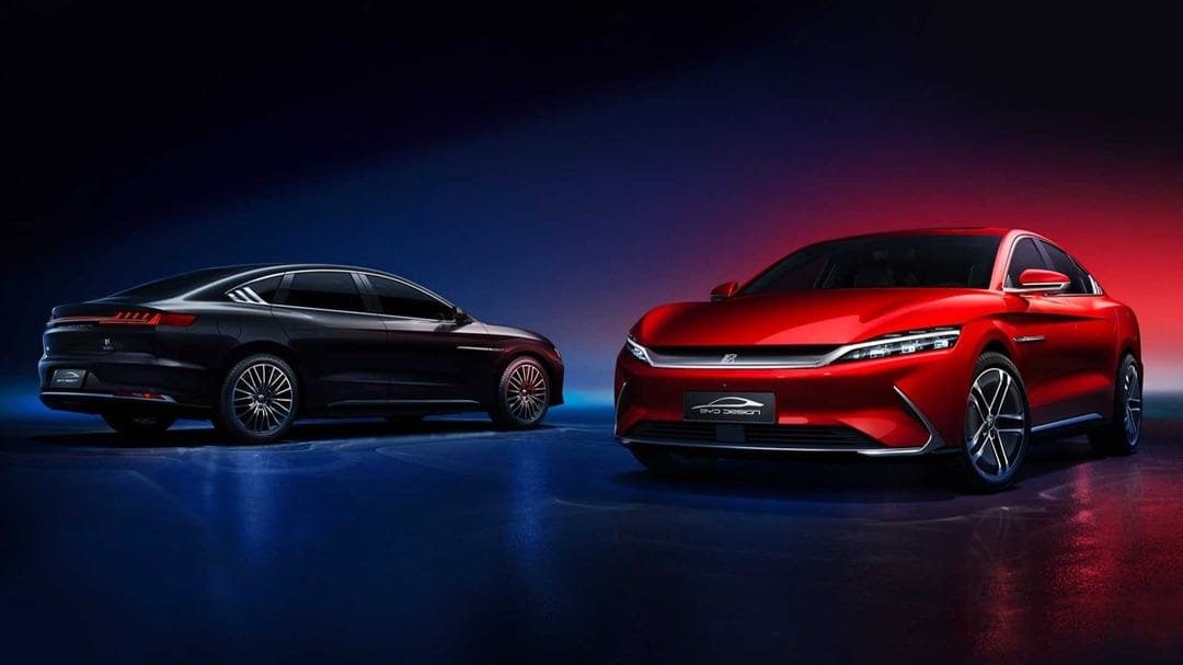 Red and black luxury electric cars displayed in a studio with dramatic blue and red neon lighting.
