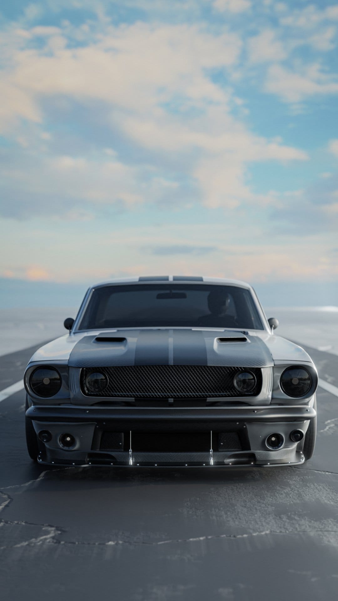 Ford Mustang GT with racing stripes drives on a coastal road under cloudy skies, seen from a front-facing angle.