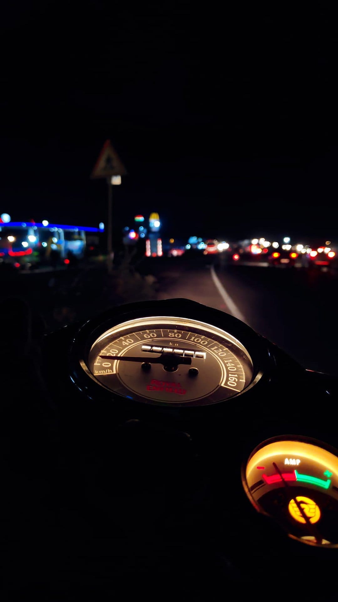 Motorcycle speedometer and dashboard gauges glow at night with blurred streetlights stretching into the distance.